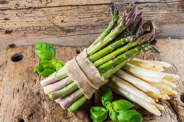 tied bunches of green and white asparagus and fresh basil leaves on wooden surface