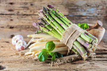 tied bunches of green and white asparagus and fresh basil leaves on wooden surface