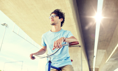 people, style, leisure and lifestyle - young hipster man riding fixed gear bike on city street