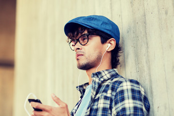 people, music, technology, leisure and lifestyle - happy young hipster man with earphones and smartphone listening to music