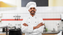 Cooking, Profession And People Concept - Happy Male Indian Chef In Toque With Crossed Arms Over Restaurant Kitchen Background