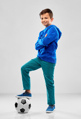 childhood, football and sport concept - smiling boy in blue hoodie with soccer ball over grey background