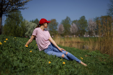 Wall Mural - Successful business woman enjoys her leisure free time in a park with blossoming sakura cherry trees wearing jeans, pink t-shirt and a fashion red cap