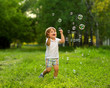 Beautiful 2 year old boy playing in the summer outside in the greenery with soap bubbles