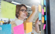 © paulaphoto - Closeup portrait of young business woman at office and use sticky notes to share ideas. Worker writing in note pad on the wall. Idea modern creative business communication brainstorming concept