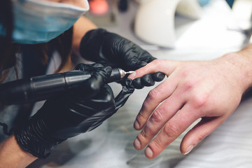 Men's manicure. Professional manicure for man by manicure machine. A man receiving a manicure in the beauty salon. Beautician master trimming and removes cuticles