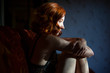 © Cavan Images - Pensive redhead woman sitting on the sofa