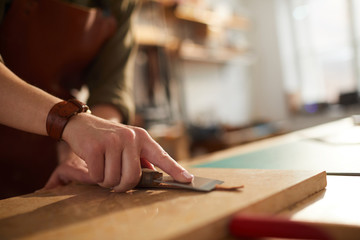 Wall Mural - Close up of unrecognizable craftsman working with leather in tannery shop lit by sunlight, copy space