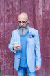 © Rafa Fernandez/ADDICTIVE STOCK - Front view of a mature trendy bearded hipster standing against a red vintage door outdoors while using a mobile phone