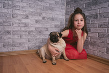 Charming Girl Sitting On Floor With Dog Smiling Cute Little Girl With Long Hair Putting Horns On Pug Dog Sitting On Floor And Looking At Camera Against Background Of Gray Brick Wall