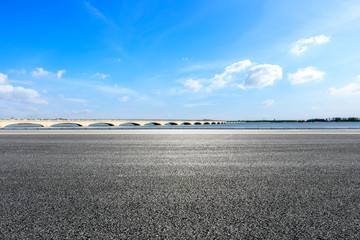 Empty asphalt road and lake with bridge under blue sky