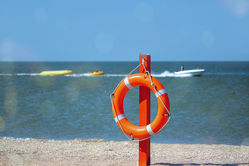 Lifebuoy orange coloredon a pillars on the beach. Against the backdrop of the sea landscape. Safety equipment. Selective focus.