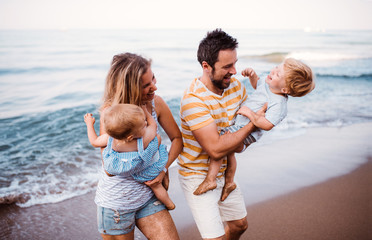 Canvas Print - A young family with two toddler children walking on beach on summer holiday.