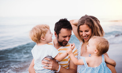 Young family with two toddler children walking on beach on summer holiday.