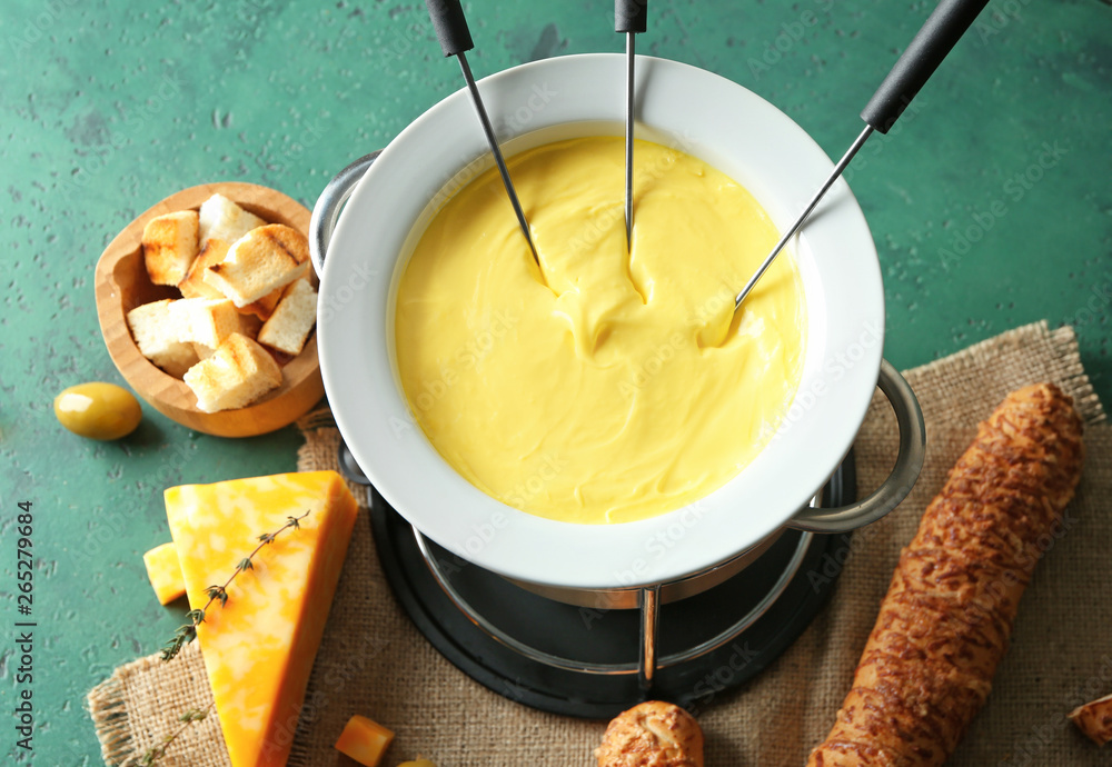 Cheese fondue with snacks on color background