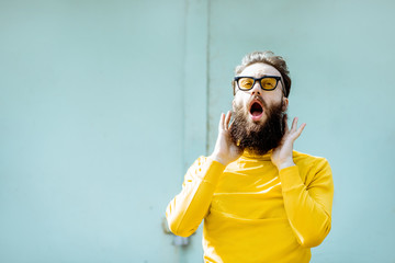 Wall Mural - Portrait of a confident stylish bearded man in yellow sweater on the turquoise background outdoors