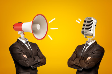 Waist-deep view of two businessmen standing in half-turn, arms folded, with megaphone and microphone instead of heads.
