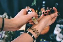 Female Applying Essential Oil On Her Wrist. Caucasian Woman Wearing Bracelets Jewelry And Black Nail Polish. Emerald Green Dark Themed Color Palette. Essential Oil On Left Hand, Applying On Right Hand