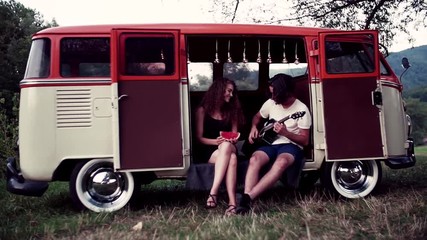 Wall Mural - A young couple at dusk outdoors on a roadtrip through countryside, playing guitar.