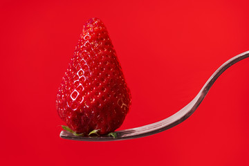 Red strawberry on fork with red display background