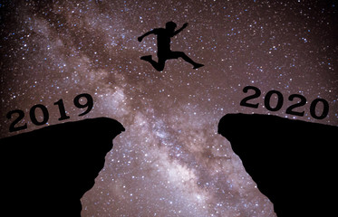 A young man jump between 2019 and 2020 years over night sky with stars and through on the gap of hill  silhouette evening colorful sky. happy new year 2020.