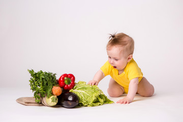 Wall Mural - baby girl smiling in yellow bodysuit on white background with vegetables, baby food concept