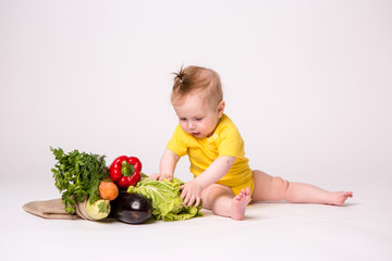 Wall Mural - baby girl smiling in yellow bodysuit on white background with vegetables, baby food concept