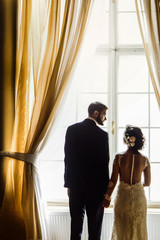 stylish luxury bride and handsome elegant groom posing in light at gorgeous window on the background of rich interior in old building