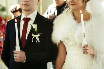 wedding ceremony of happy elegant blonde bride and stylish groom, holding candles in the old church