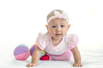 Little baby Asian girl 7 months with pink dress looking at camera on white bed.