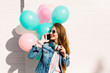 Stylish cheerful girl in sunglasses waiting for party start and speaking to friend by the phone. Adorable young woman in headphones carrying balloons came to congratulate mother with her birthday.