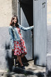 © sonyachny - stylish brunette beautiful woman posing and smiling in floral dress near wooden door in the street