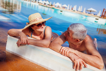 Wall Mural - Senior couple relaxing in swimming pool. People enjoying summer vacation.