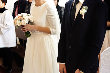 happy stylish bride and elegant groom sitting at catholic wedding ceremony at church