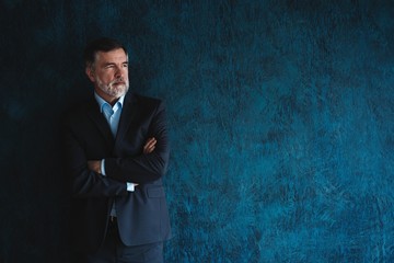 Serious mature man posing in front of a dark blue background with copy space.