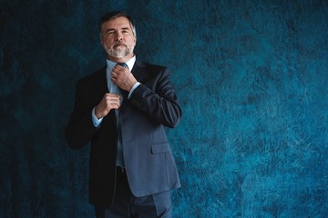 Wall Mural - Serious mature man posing in front of a dark blue background with copy space.