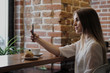 © spaskov - A young beautiful brunette girl in a loft-style cafe sits at a table by the window, drinks coffee and uses a smartphone, calls, takes pictures.