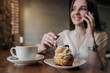 © spaskov - A young beautiful brunette girl in a loft-style cafe sits at a table by the window, drinks coffee and uses a smartphone, calls, takes pictures.