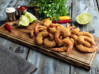 Wall Mural - fried breaded shrimps served with lime and coriander leaves on wooden board, delicious deep, red, white sauce