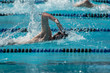 © colloidial - A young man swimming freestyle.  Bright sun, deep blue pool water.  Taking a breath, high elbow.  Splashing water.