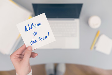 Wall Mural - Woman clerk sitting holding note paper sticker with welcome to the team phrase. Business concept. Concept.