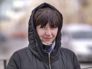 Portrait of a young woman in a hood on a city street, looking at the camera