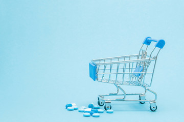 pills and shopping trolley on blue background. creative idea for health care cost, drugstore, health