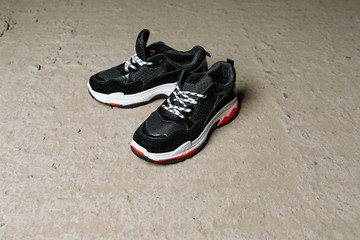 black sneakers on thick white with red accents soles on a gray concrete background