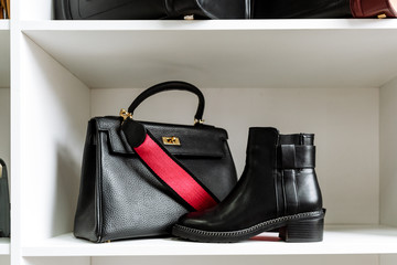 pair of black leather shoes with low heels and a black bag with a gold buckle and a red belt on a white shelf in the store