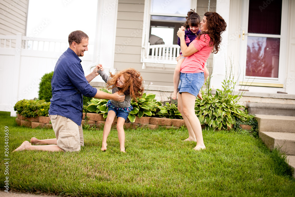 Happy family playing together in their yard in front of their beautiful home