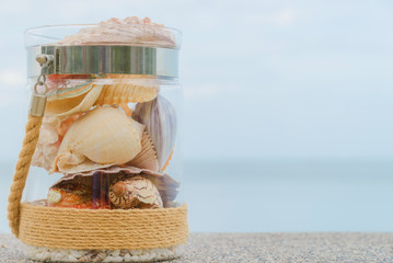 Wall Mural - Variety of sea shells in glass jar and seascape on background with copy space. holiday concept