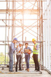 © Sura Nualpradid - Group of engineers, man and woman, working together in construction site, standing on bridge among the scaffold, orange sun light in background.