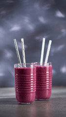 Glasses full of violet smoothie with two straws on gray table