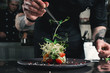 © Mykola - Chef finishing healthy salad on a black plate with tweezers. almost ready to serve it on a table